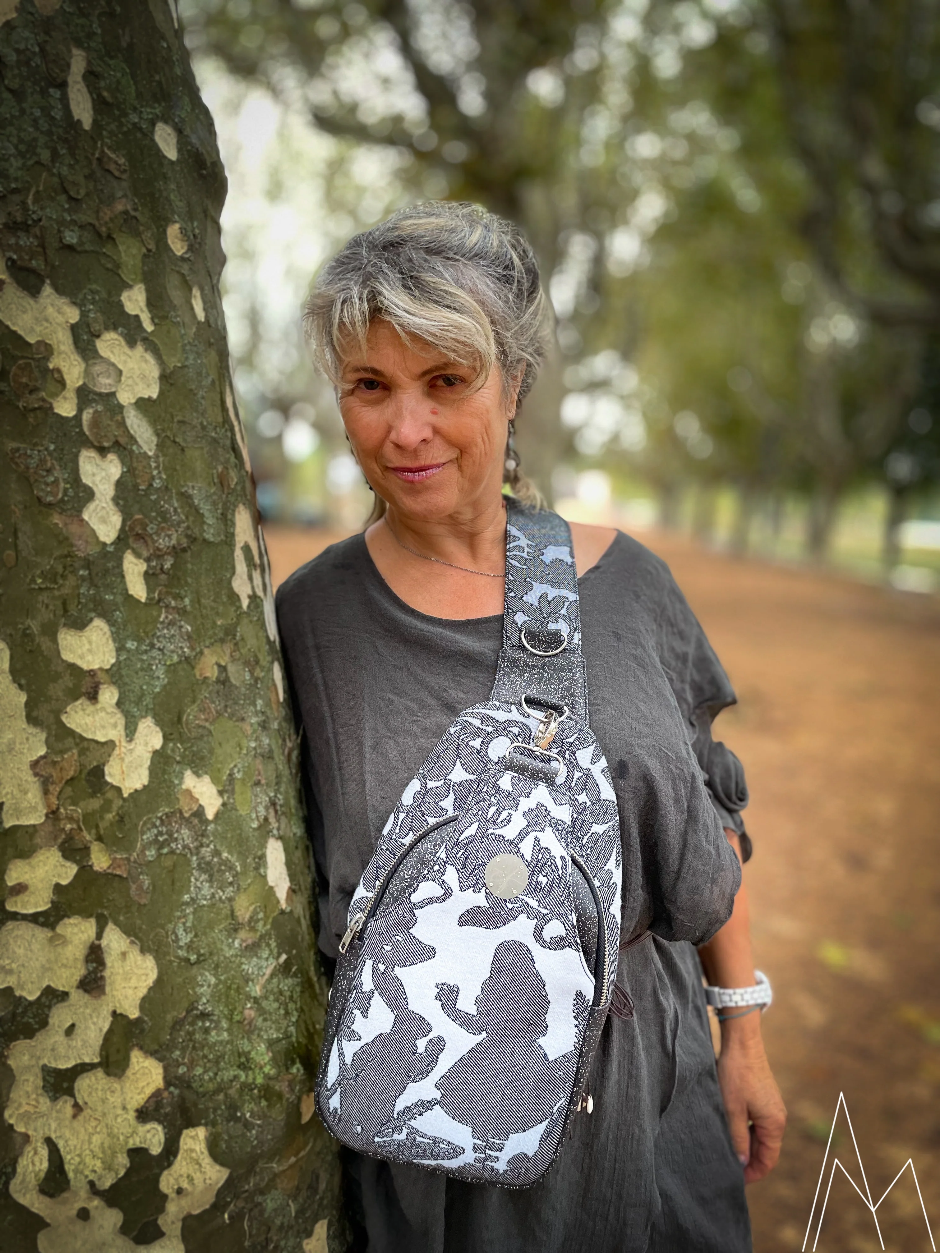 Photo of a mature woman carrying a gray and blue backpack by hand, in an outdoor park during the day.