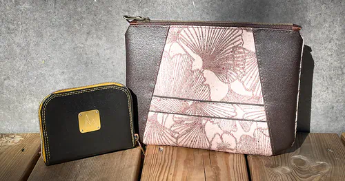 Pyramide N-07 pouch and Mini En Ville Millésime 2022 wallet in Nisiar grape marc leather, placed on a wooden terrace.
