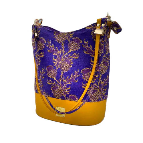 A bucket bag made from babywearing wrap fabric featuring yellow thistles on a purple background with yellow lamb leather.