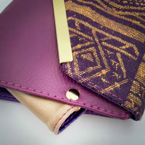 A wallet made from purple and yellow geometrical patterned wrap scrap combined with purple and gold reclaimed faux leathers on the outside, and mustard flax light canvas and deep violet satin on the inside.
