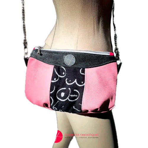 A messenger bag made from a black and white babywearing wrap with stylized breast drawings, black stingray leather, and pink stingray leather.