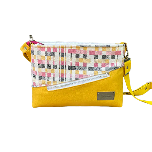 A rectangular messenger bag made from black, white, pink, and yellow babywearing wrap fabric with a geometric pattern, and sunflower yellow faux leather.