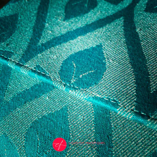 A flat handbag with a flap made from cream and turquoise babywearing wrap with stylized leaf pattern.