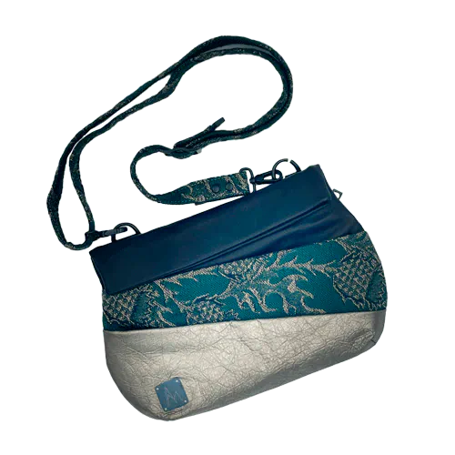 A shoulder bag made from two leathers, gold and black, and a piece of baby wrap fabric in black, green, and gold with a thistle pattern on the outside, and forest green poplin and gold satin on the inside.