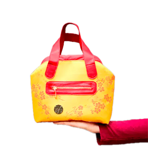 A mini handbag made of yellow upholstery fabric with a red cherry blossom pattern and red leather.