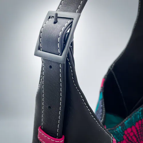 A shoulder bag made from a wax-style fabric and scraps of black and pink leather, lined with turquoise fabric.