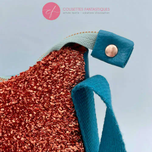 A zippered small shoulder bag made from stretch fabric with copper metallic bouclé, turquoise blue faux leather, and bright light orange lining.