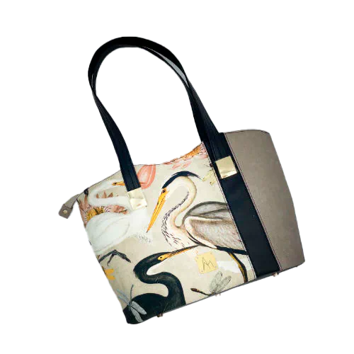 A large zippered shoulder bag, reminiscent of a tote, made from a thick fabric with a wild bird pattern, combined with black and taupe faux leather, and lined with mottled cream linen and coral.