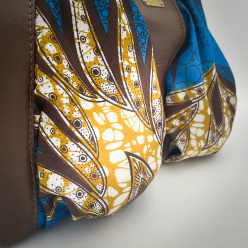 A shoulder bag made of brown goat leather, blue and mustard wax fabric, and mustard-yellow lining.