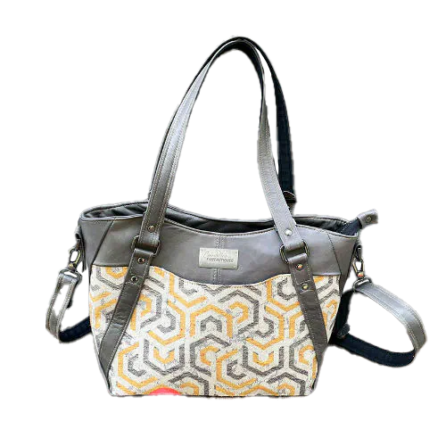 A shoulder bag made from gray, mustard, and ecru babywearing wrap with geometric patterns, and gray lamb leather.
