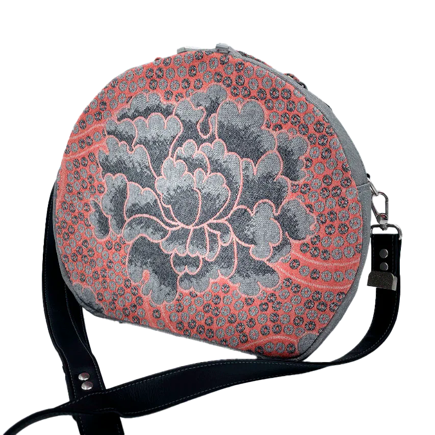 A round shoulder bag made of gray glitter vinyl canvas, with a vintage floral patterned pink and gray baby sling scrap and a gray satin lining.