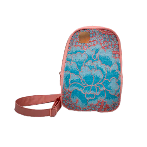 A backpack made of peach-colored faux leather and a babywearing wrap in shades of pink and turquoise with a vintage floral pattern.