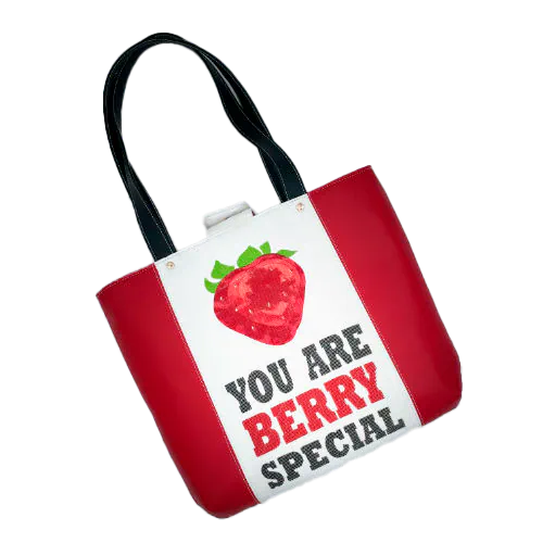 A large bag made from red faux leather on the outside and a canvas printed with a fruit design with an English pun underneath, and on the inside a bright red poplin.