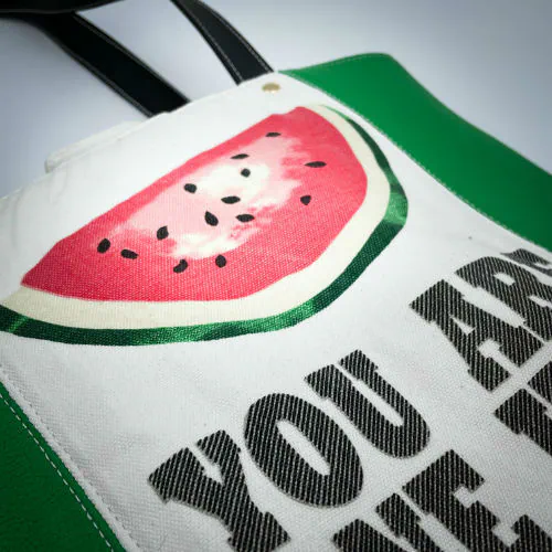 A large bag made from green leather on the outside and a canvas printed with a fruit design with an English pun underneath, and on the inside a forest green poplin.