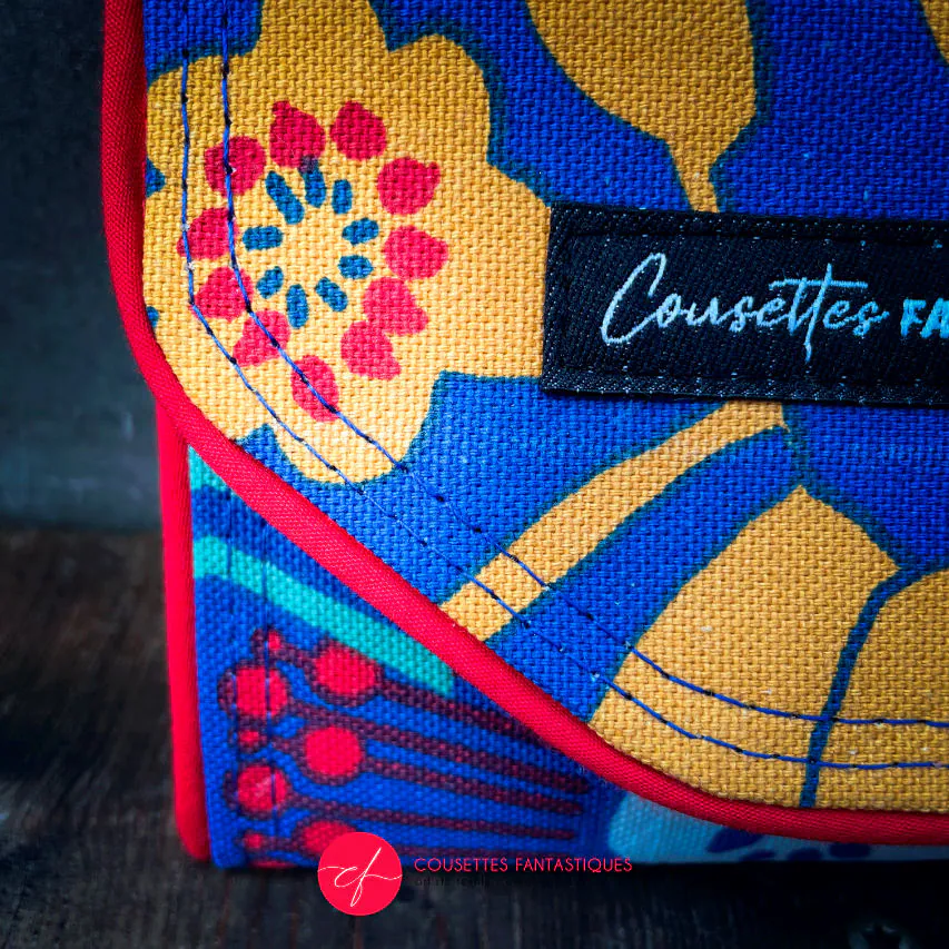 Un portefeuille fait en toile bleue roi à motifs floraux jaunes, blancs et rouges à l'extérieur et toiles unies jaune et rouge à l'intérieur.