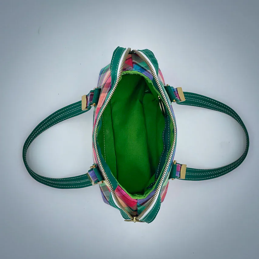 Un sac portefeuille constitué de cuir vert forêt et de toile de madras multicolore.