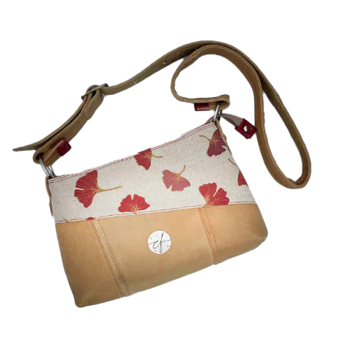 Une besace rectangulaire faite de cuir de couleur camel et d'une toile en polycoton avec un motif de feuilles de Ginkgo Biloba rouges.