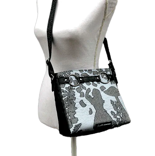 Un sac en bandoulière trapézoïdal fabriqué à partir d'une écharpe de portage “Alice au pays des merveilles” en noir, bleu-gris et argent, associée à un simili noir matelassé à la main.