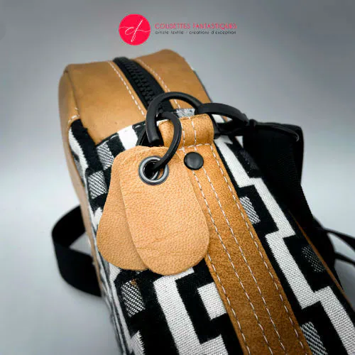 Un sac en bandoulière fabriqué à partir d'une écharpe de portage à motif géométrique noir et blanc, de cuir caramel et de popeline rouge.