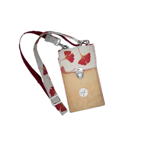 Une pochette-téléphone cousue dans un cuir de couleur camel et une toile en polycoton avec un motif de feuilles de Ginkgo Biloba rouges.