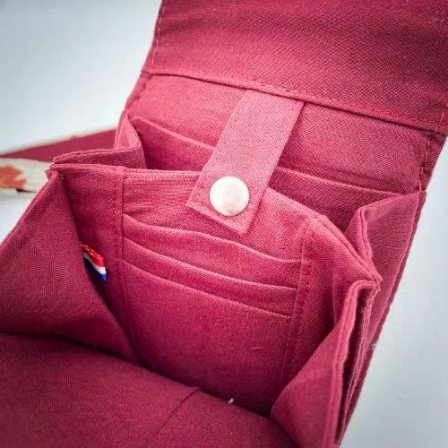 Une pochette-téléphone cousue dans un cuir de couleur camel et une toile en polycoton avec un motif de feuilles de Ginkgo Biloba rouges.