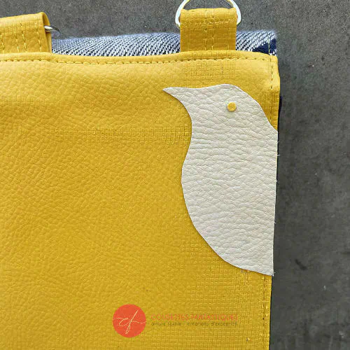Un portefeuille fabriqué à partir d'une écharpe de portage grise, bleu marine et jaune avec des motifs d'oiseaux, et du simili jaune soleil.