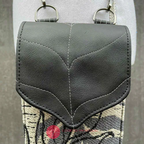 Un compagnon fabriqué à partir d'une écharpe de portage blanche, noire et grise avec des motifs de feuilles tropicales et un simili cuir noir.
