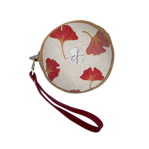 Une pochette ronde faite de cuir de couleur camel et d'une toile en polycoton avec un motif de feuilles de Ginkgo Biloba rouges.