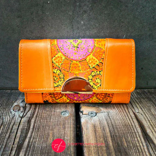 Un portefeuille fabriqué en cuir d'agneau orange et en tissu vintage multicolore en rayonne, dans des tons d'orange, de jaune et de rose.