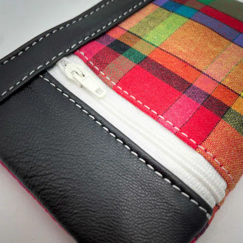 Un petit porte-monnaie zippé fabriqué à partir d'un patchwork de différents matériaux : une toile de Madras et du cuir d'agneau noir.