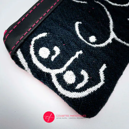 Un petit porte-monnaie zippé fabriqué à partir d'un patchwork de différents matériaux : une écharpe de portage noir et blanc avec un motif stylisé de seins, du cuir d'agneau noir et du simili fuchsia.