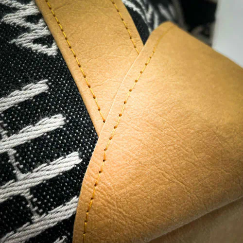 Un petit sac de voyage fabriqué en papier lavable couleur caramel, une écharpe de portage à motif géométrique noir et blanc, et de la popeline grise.