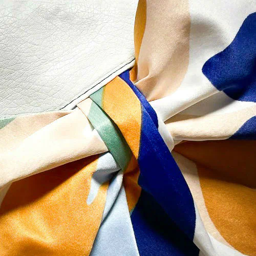 Une petite pochette zippée cousue en similicuir blanc et une écharpe colorée avec un design floral moderne et abstrait en blanc, bleu, sauge, beige et cannelle. À l'intérieur se trouve un popeline brillant de couleur sauge claire.