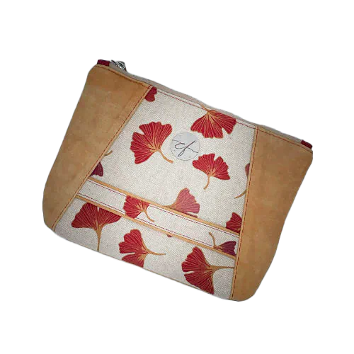 Une pochette zippée cousue dans un cuir de couleur camel et une toile en polycoton avec un motif de feuilles de Ginkgo Biloba rouges.