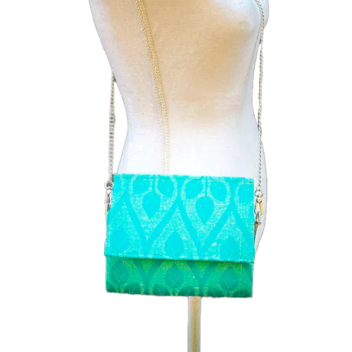 Un sac à main plat avec un rabat en écharpe de portage crème et turquoise avec motif de feuilles stylisées.