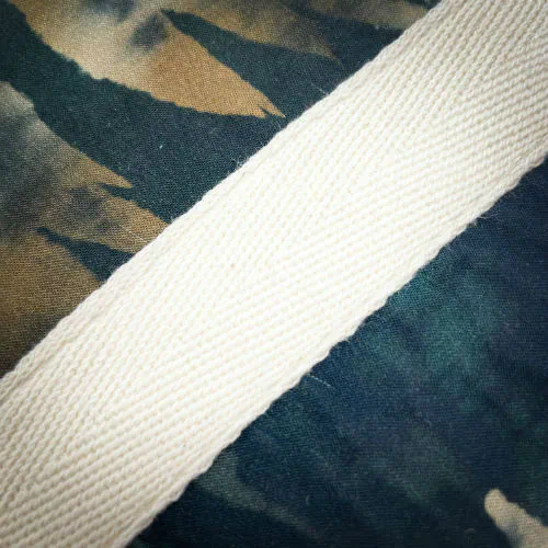 Une pochette zippée double cousue dans une suédine synthétique beige et un tissu au motif abstrait dans les tons vert forêt, beige et fauve, doublé d'une popeline vert amande.