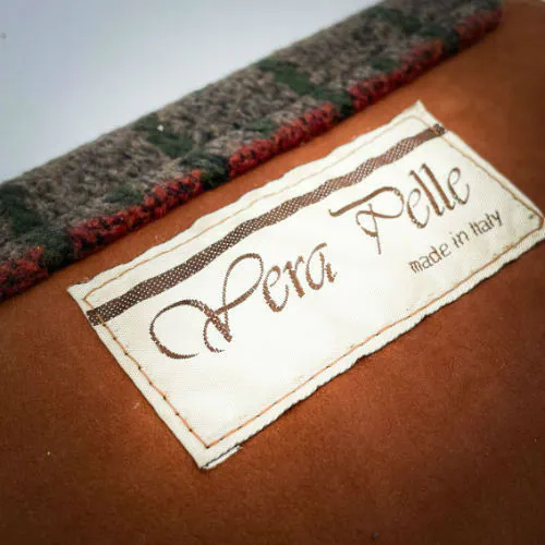 Un portefeuille fabriqué à partir de en suédine alezan et drap laine au motif géométrique, avec une doublure en viscose à motif géométrique.