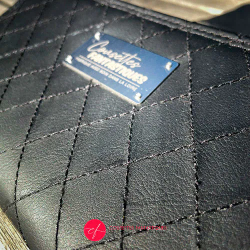 Un porte-cartes-et-monnaie zippé fabriqué avec du simili noir matelassé à la main à l'extérieur, et de la toile de coton avec des paillettes à l'intérieur.