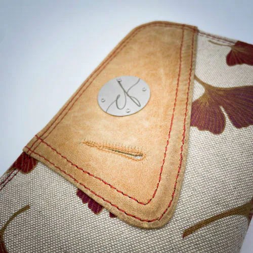 Un porte-cartes-et-monnaie zippé fait de cuir de couleur camel et d'une toile en polycoton avec un motif de feuilles de Ginkgo Biloba rouges.
