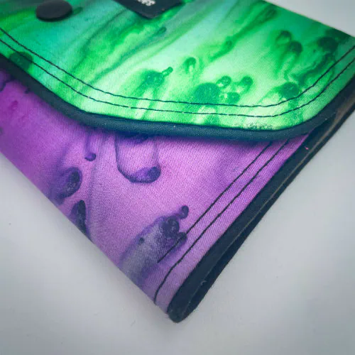 Un portefeuille fait en voile de soie bleu, vert et violet associé à du cuir d'agneau noir à l'extérieur, et en popeline taupe à l'intérieur.