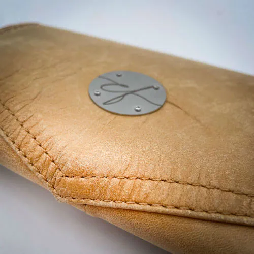 Un portefeuille fabriqué avec du cuir de couleur camel et une toile en polycoton avec un motif de feuilles de Ginkgo Biloba rouges.