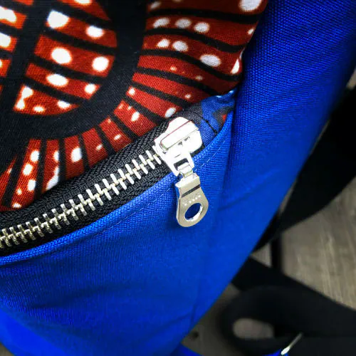 Un sac à dos cousu en toile bleu roi et tissu wax dans les tons bleus, marron-rouge, noir et blanc.