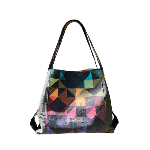 Un sac d'épaule fabriqué avec une écharpe de portage noire à motif géométrique arc-en-ciel et du liège noir, avec un intérieur en tourbillon arc-en-ciel lumineux.