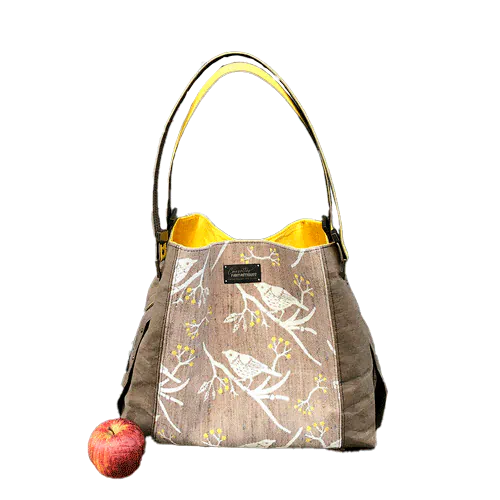 Un sac d'épaule fait à partir de papier lavable couleur chocolat, écharpe de portage beige rosé chiné, au motif d'oiseaux blancs dans des branchages blancs et jaune, avec une doublure jaune vif.