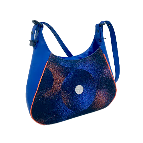 Un sac d'épaule zippé, fabriqué à partir de chutes d'une écharpe de portage noir, bleu, rose et orange et de simili bleu royal, et doublé d'une doublure orange vif lumineuse.
