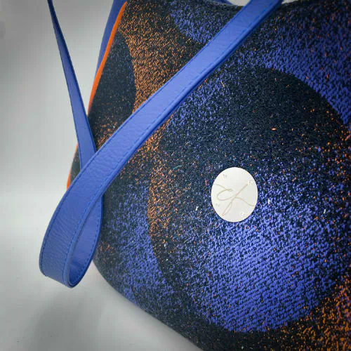 Un sac d'épaule zippé, fabriqué à partir de chutes d'une écharpe de portage noir, bleu, rose et orange et de simili bleu royal, et doublé d'une doublure orange vif lumineuse.