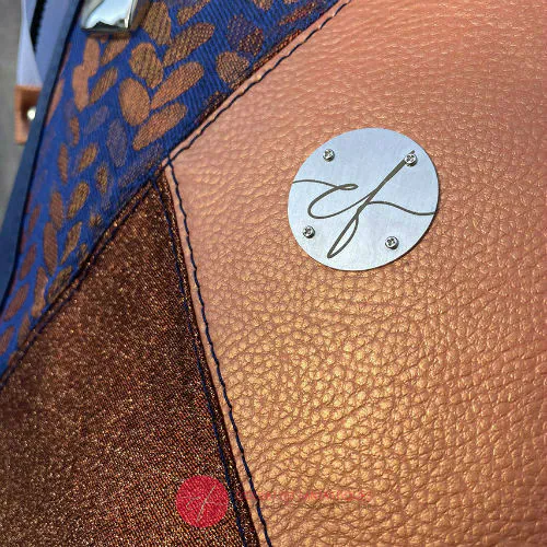 Un sac d'épaule composé d'un patchwork de différents matériaux : similicuir bleu royal, similicuir doré, tissu brillant bronze, et tissu wrap bleu et bronze avec un motif de petites gouttes.