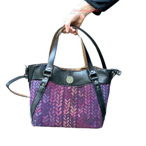 Un sac d'épaule fait en tissu dans les tons violets, pourpres, roses... au motif de goutelettes, et de cuir d'agneau noir upcyclé.