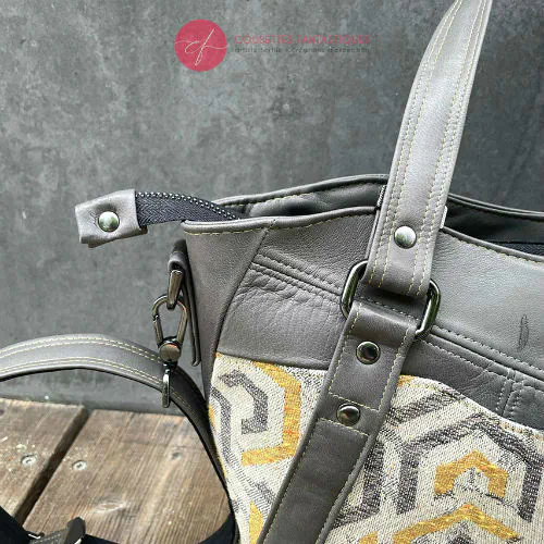 Un sac d'épaule fait en écharpe de portage gris, moutarde et écru avec motifs géométriques, et cuir d'agneau gris.