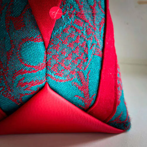 Un sac d'épaule fait avec du tissu d'écharpe rouge sang et vert émeraude au motif de chardons, de la gabardine rouge, de la toile de lin vert émeraude et du simili rouge.